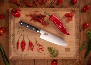 KOTAI Hashi Santoku met 17 cm lemmet op snijplank naast rode pepers