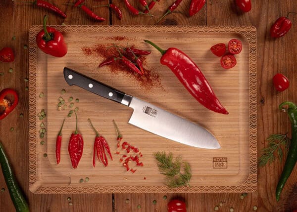 KOTAI Hashi Santoku met 17 cm lemmet op snijplank naast rode pepers